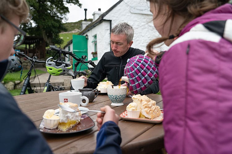 Three mountain bikers drinking tea and eating traybakes at Carrick Cottage, Mourne Mountains