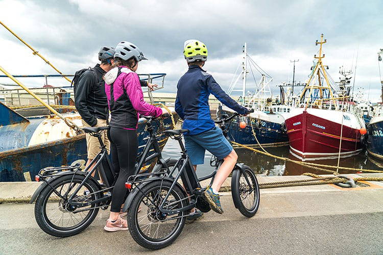 Three family members on ebikes exploring the harbour in Kilkeel with bright coloured fishing boats in the background
