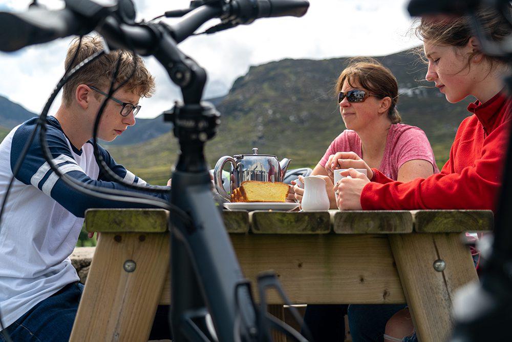 Young teenagers drinking tea and eating traybake with their mother at Meelmore Lodge, Trassey Valley in the Mourne Mountains