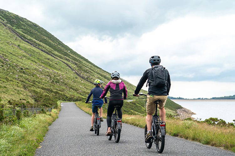 Three bikers cycling along the road at Ben Crom Dam, Silent Valley, Mourne Mountains